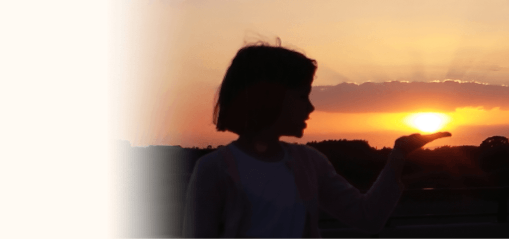 Girl appearing to hold the sun in her hand at sunset